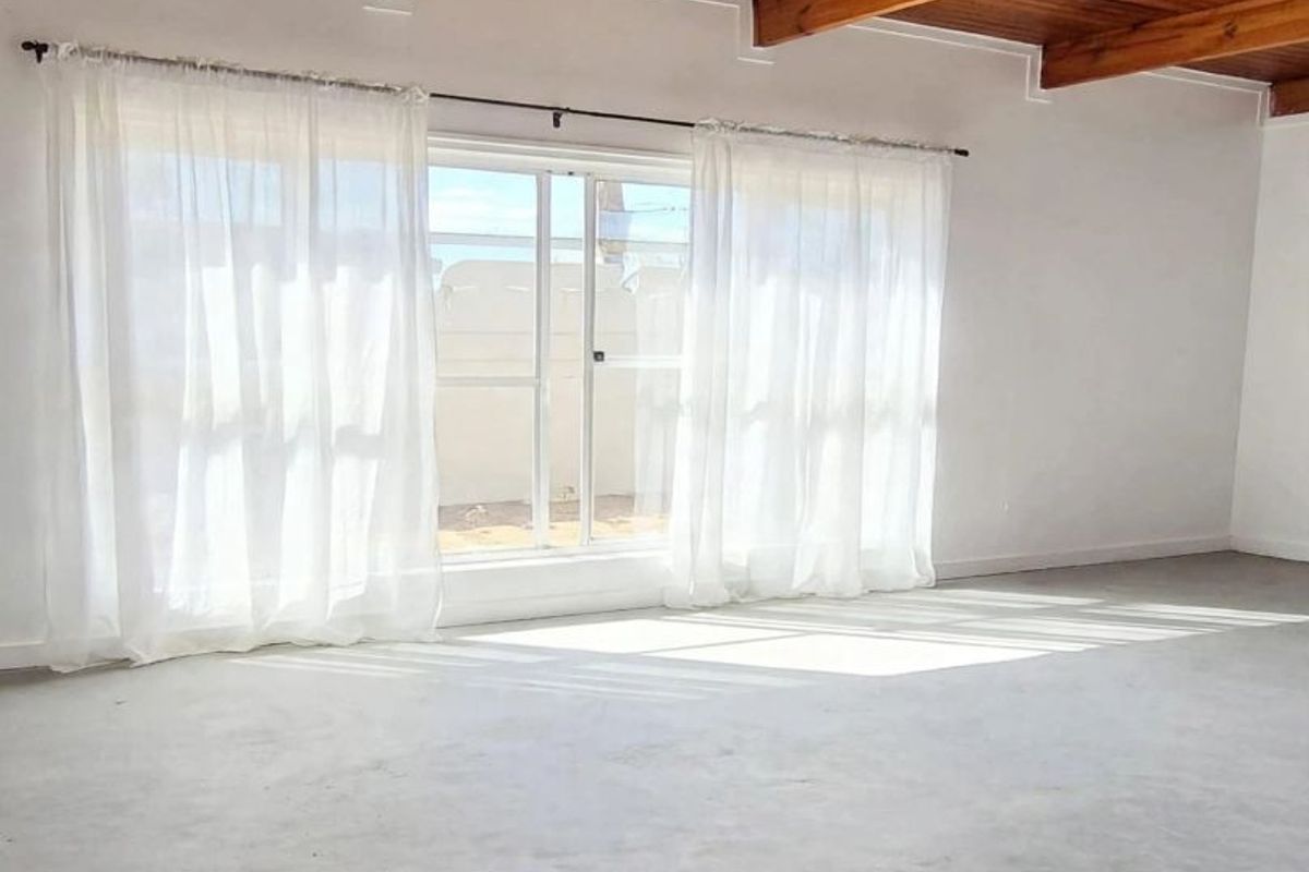 Spacious living area featuring a high exposed timber beam ceiling, polished concrete flooring, and a large sliding glass door providing natural light.