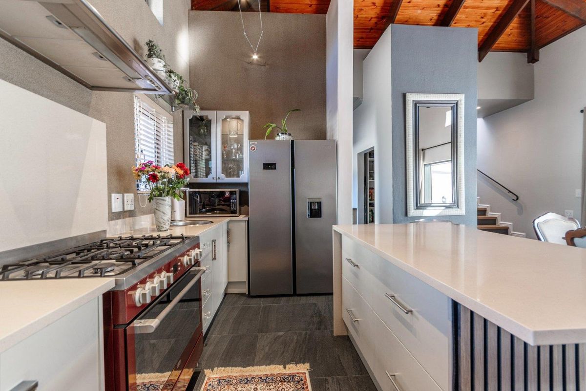 Modern kitchen featuring a gas stove, stone countertops, a central island, and exposed timber ceiling beams, creating a warm and functional culinary space.
