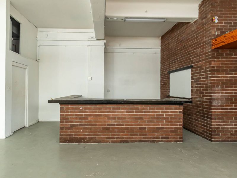 An empty interior space featuring a built-in brick bar counter, exposed brickwork, and industrial-style exposed ceiling beams.