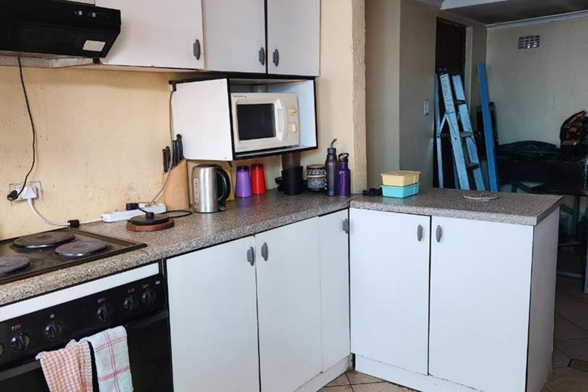 A functional kitchen featuring white cabinetry, laminate countertops, and an integrated stove with extractor fan, finished with ceramic floor tiles and coving.