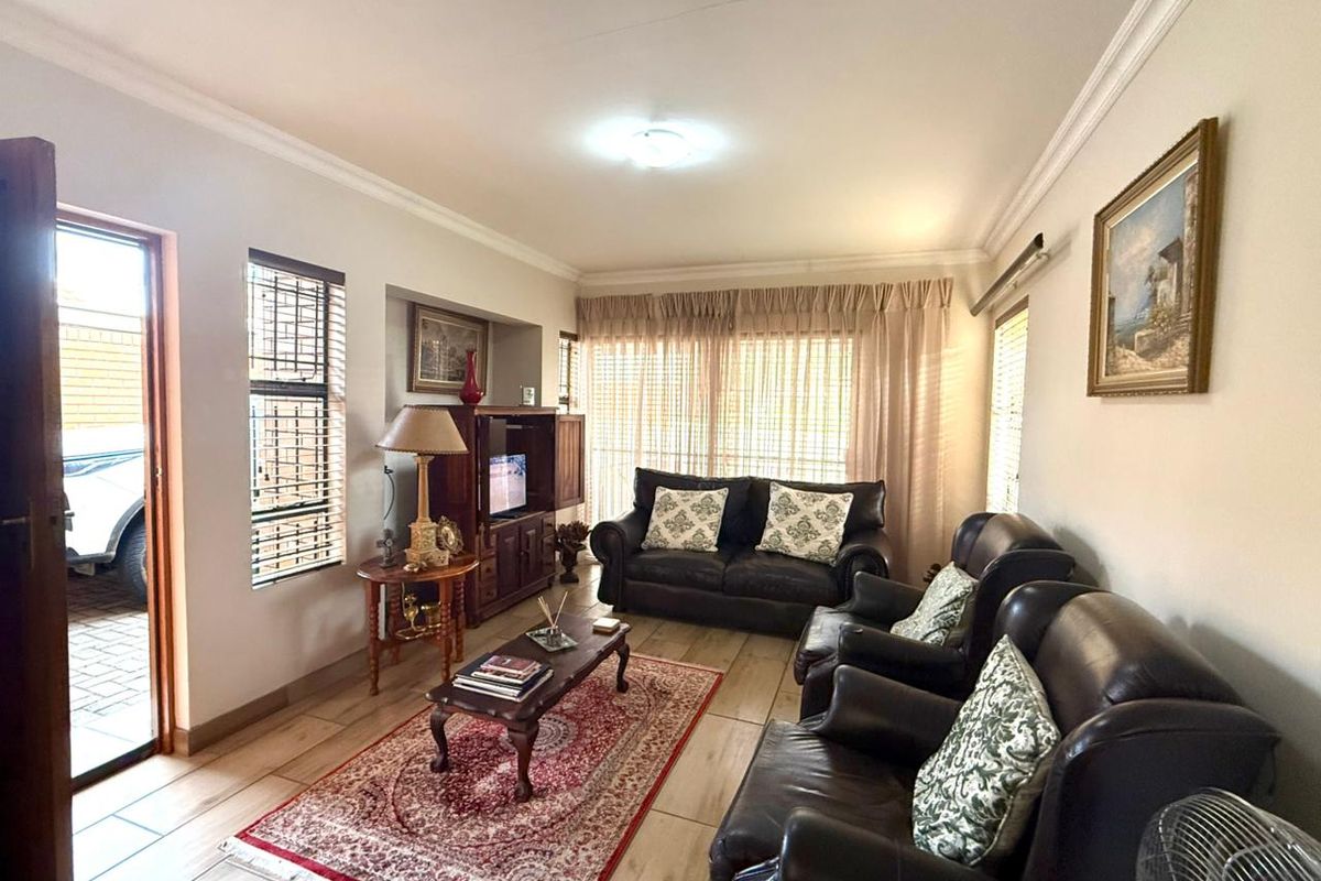 A comfortable living room featuring tiled flooring, crown molding, and large windows with blinds, providing natural light and direct access to the exterior.