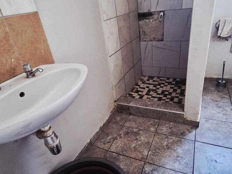 A functional bathroom featuring a wall-mounted basin, a shower cubicle with damaged tiling, and a standard toilet, requiring cosmetic updates and repairs.