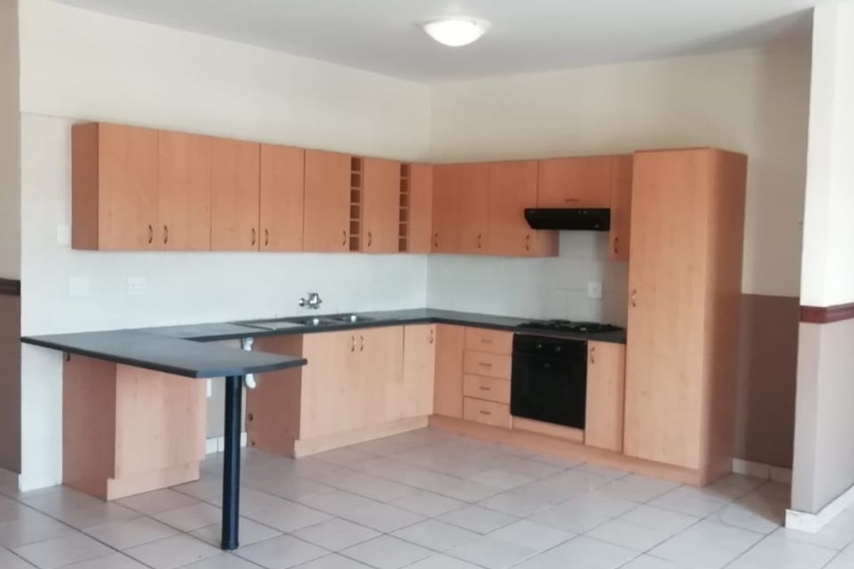 A functional kitchen featuring light wood-finish cabinetry, dark countertops, built-in oven, hob, and extractor fan, set against a neutral tiled floor.