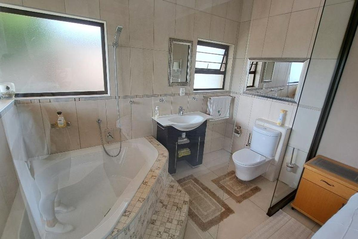 A tiled bathroom featuring a corner bathtub with shower attachment, a modern vanity basin, and a wall-mounted toilet.