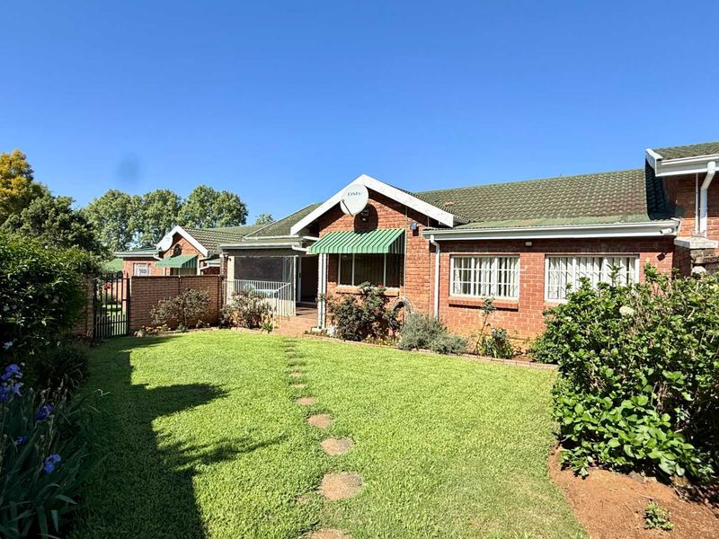 A well-maintained rear exterior view of the townhouse featuring a face brick facade, tiled roof, and a private garden with a lawn.