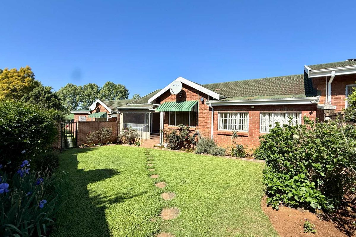 A well-maintained rear exterior view of the townhouse featuring a face brick facade, tiled roof, and a private garden with a lawn.