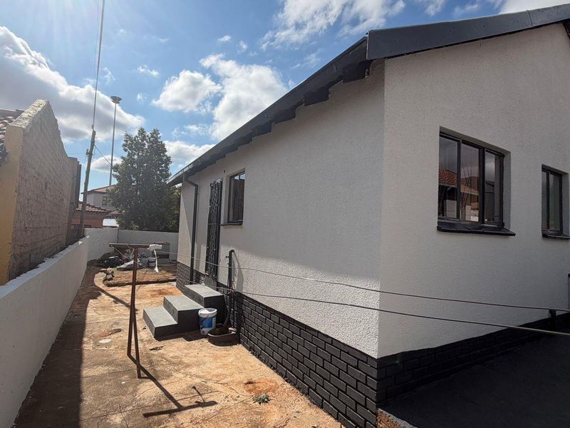 Rear view of the house featuring a textured plaster finish, brick plinth, and concrete steps leading to a side entrance.