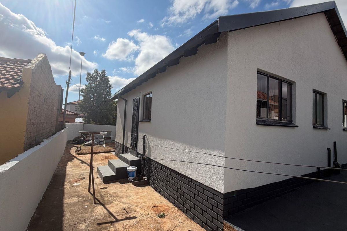 Rear view of the house featuring a textured plaster finish, brick plinth, and concrete steps leading to a side entrance.