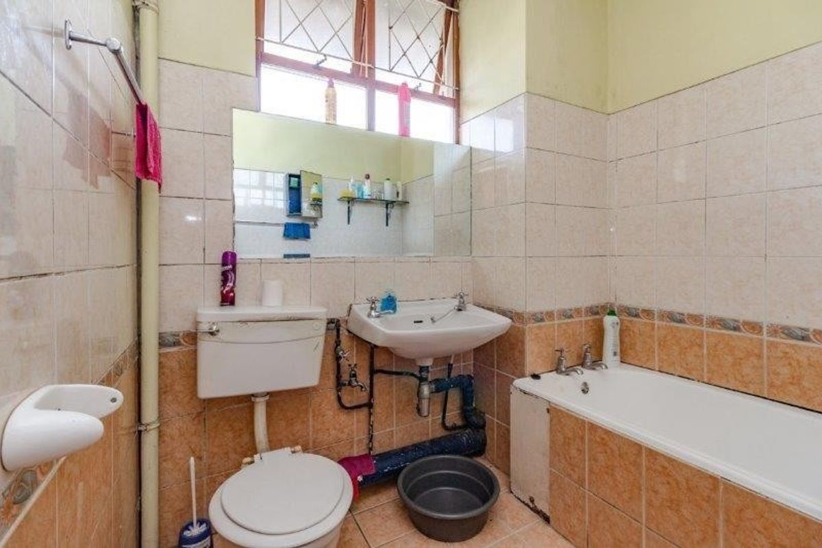 A dated bathroom featuring ceramic wall and floor tiles, a standard bathtub, pedestal washbasin, and flush toilet, requiring modernization and plumbing maintenance.