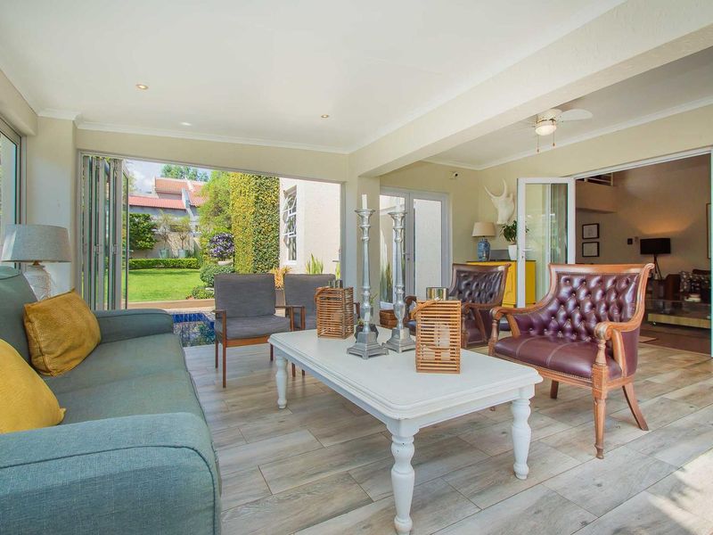 A bright, covered patio featuring modern tiled flooring, recessed lighting, and large stacking doors that open seamlessly to the garden and pool area.