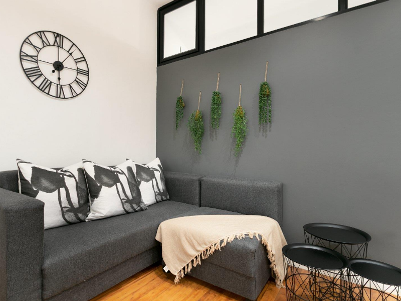 A cozy living area featuring warm hardwood flooring and a high-level transom window, accented by a modern grey feature wall.