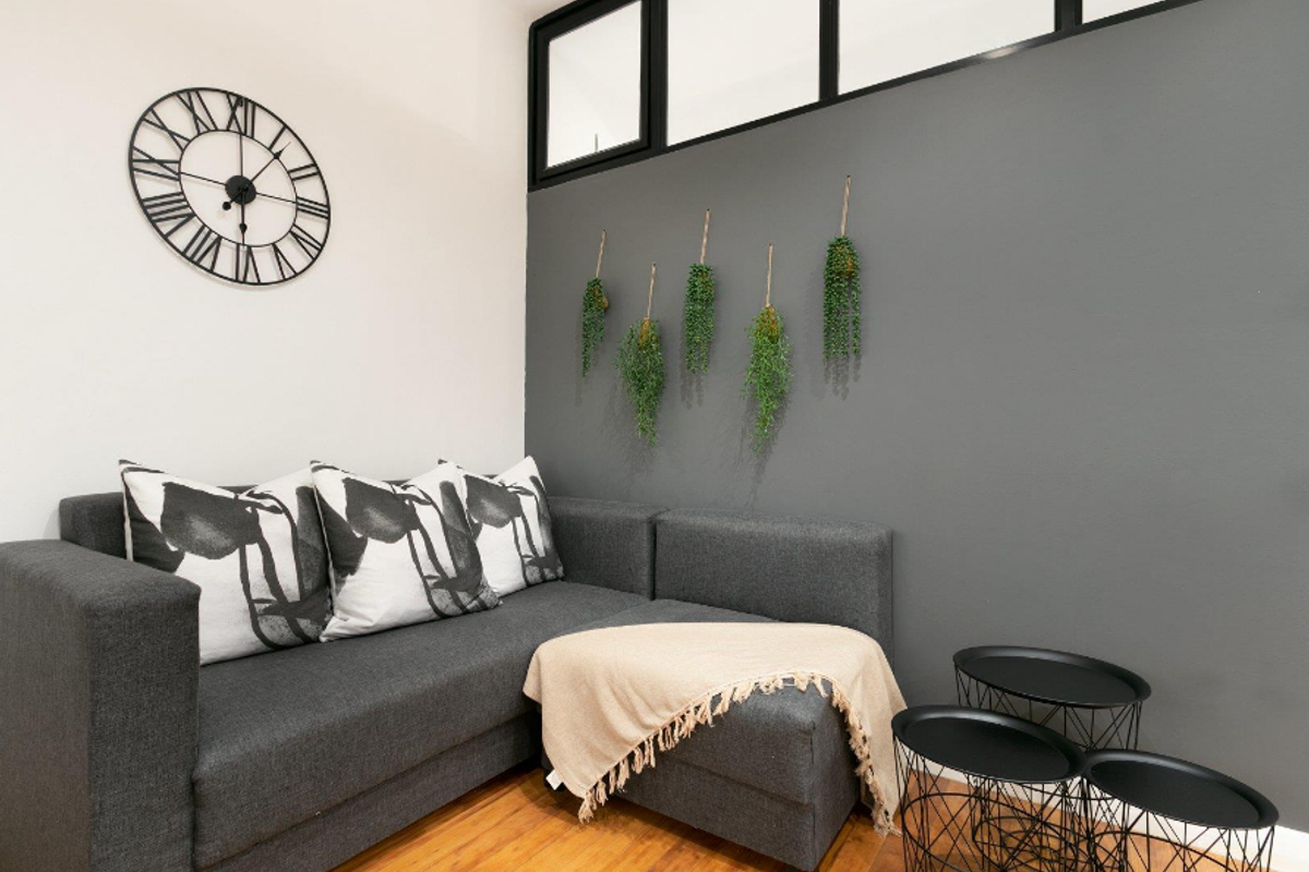 A cozy living area featuring warm hardwood flooring and a high-level transom window, accented by a modern grey feature wall.