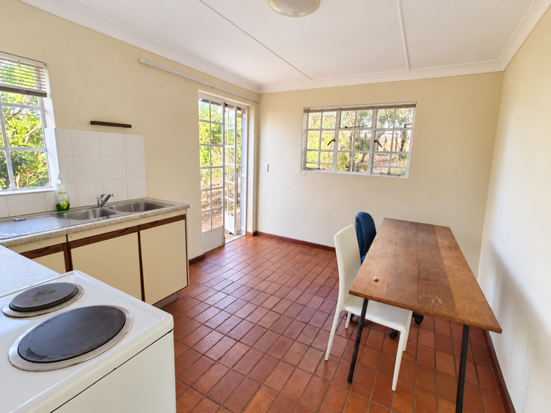 A functional kitchen featuring terracotta floor tiles, built-in cabinetry with a stainless steel sink, and direct access to the garden through a french door.