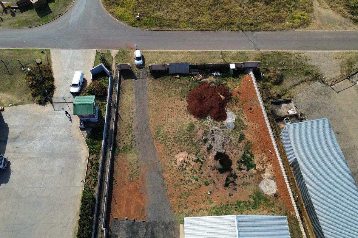Aerial view of a vacant commercial land plot featuring perimeter fencing, gated access, and a paved driveway section.