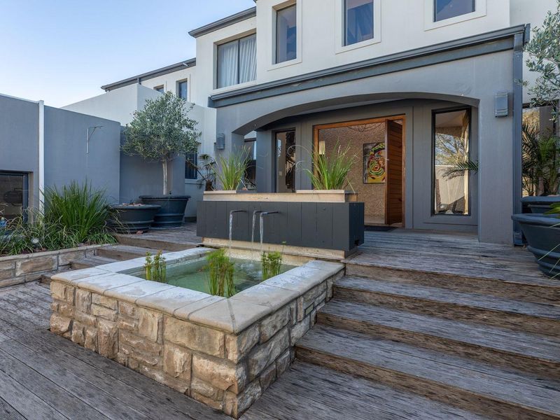 Rear exterior view featuring a timber deck, stone-clad water feature, and direct access to the main residence.