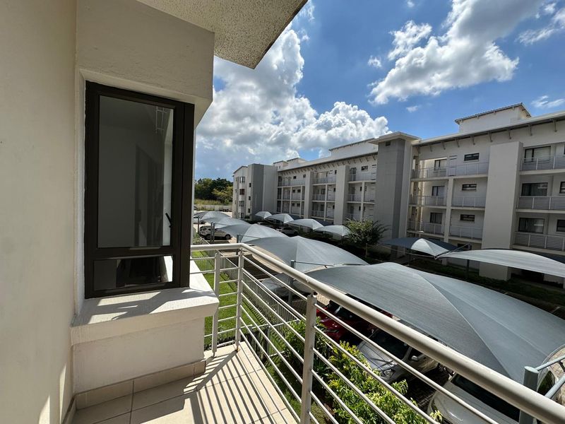 A private balcony overlooking the apartment complex parking area, featuring a metal balustrade and tiled flooring.