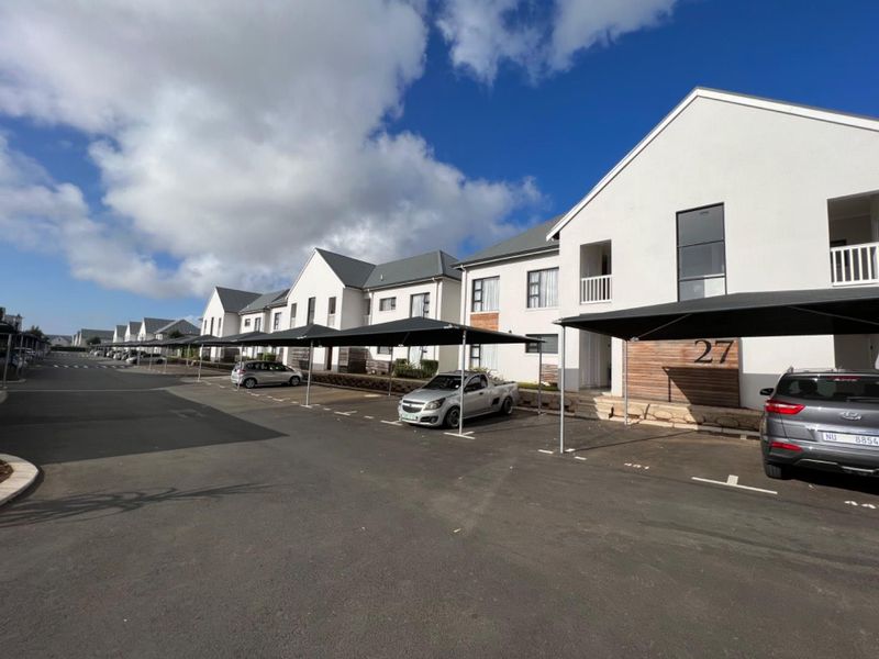 Exterior view of a modern apartment complex featuring paved parking areas with shade-cloth carports and contemporary building facades.