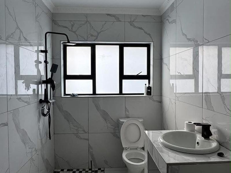 Modern bathroom featuring marble-effect wall tiles, a black shower fixture, a built-in vanity with a ceramic basin, and a distinctive checkered floor tile section.