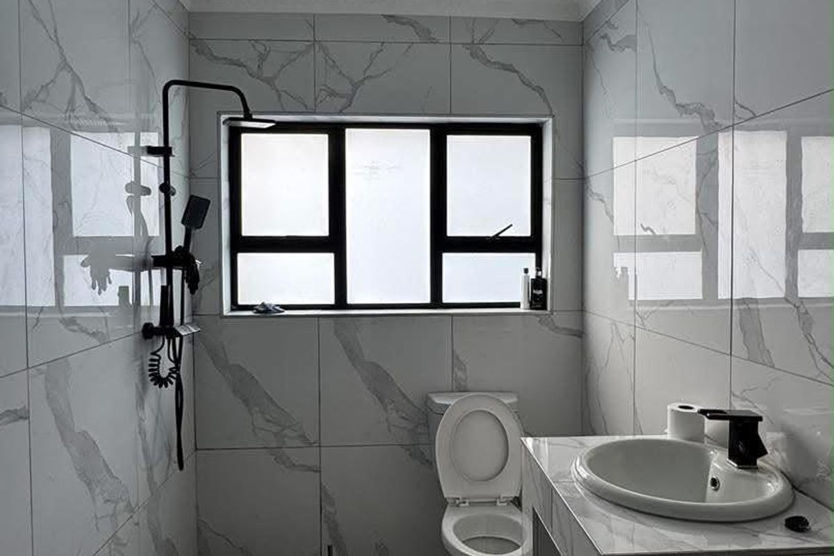 Modern bathroom featuring marble-effect wall tiles, a black shower fixture, a built-in vanity with a ceramic basin, and a distinctive checkered floor tile section.
