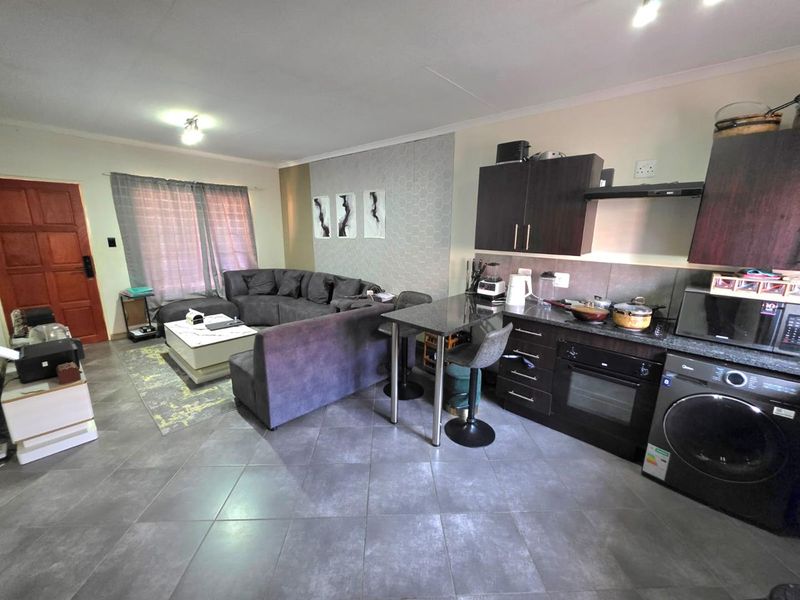 Open-plan living area featuring a modern kitchen with dark cabinetry, granite countertops, built-in oven, and tiled flooring throughout the combined space.