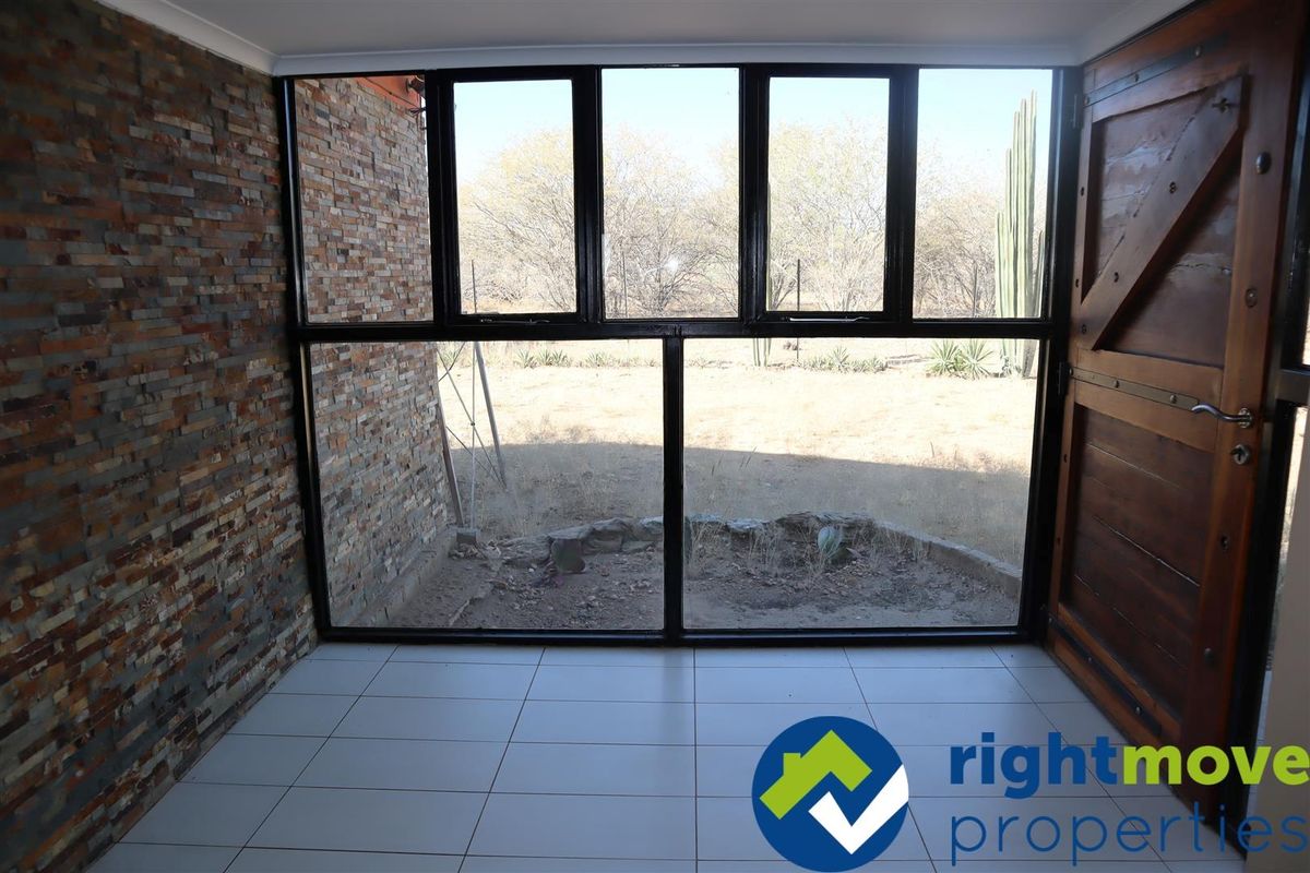 A sunlit room featuring large black-framed windows, tiled flooring, and a decorative stone-clad feature wall, offering a clear view of the outdoor landscape.