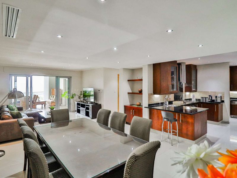 Spacious open-plan living and dining area featuring a modern kitchen with granite countertops, built-in cabinetry, and seamless access to a private balcony.