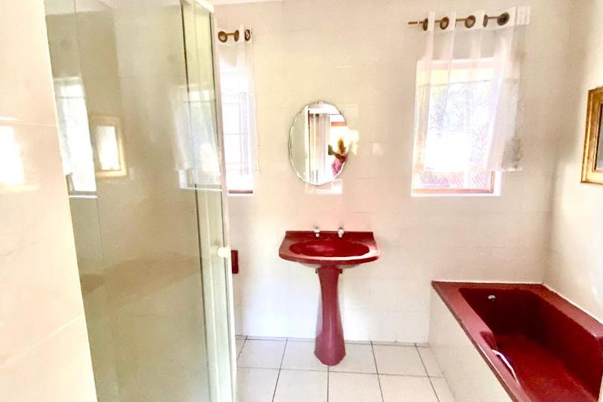 A dated bathroom featuring a red pedestal basin and matching built-in bathtub, alongside a separate shower enclosure with tiled finishes throughout.