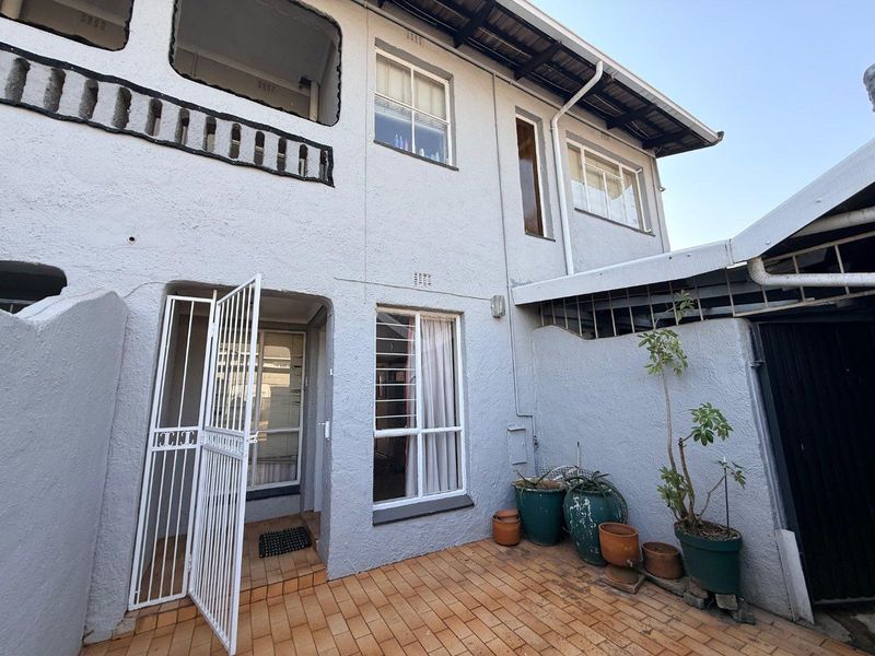 Rear exterior view of the townhouse featuring a tiled patio area, security gate, and multi-level facade with metal roofing.