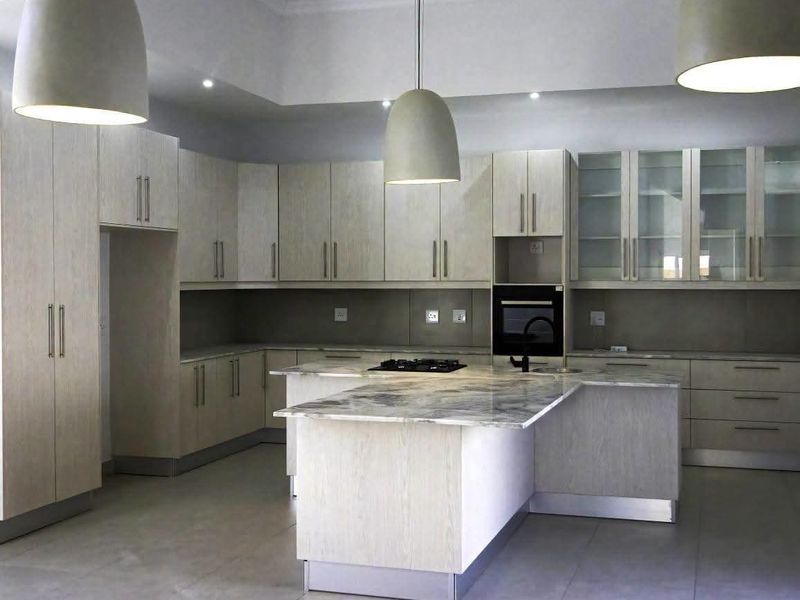 Modern kitchen featuring light wood-grain cabinetry, stone countertops, a central island with a gas hob, and elegant pendant lighting.