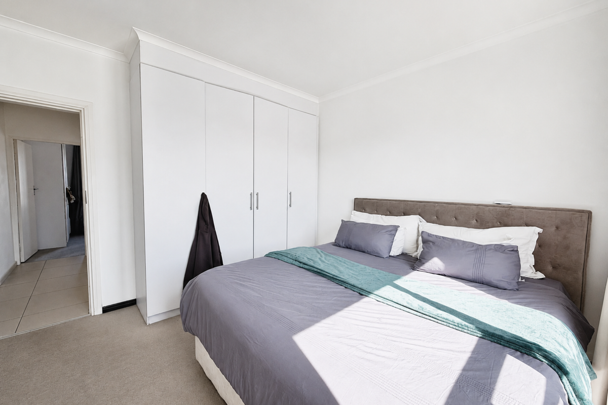 A well-maintained bedroom featuring neutral carpeting, a coved ceiling, and ample built-in cupboard storage space.