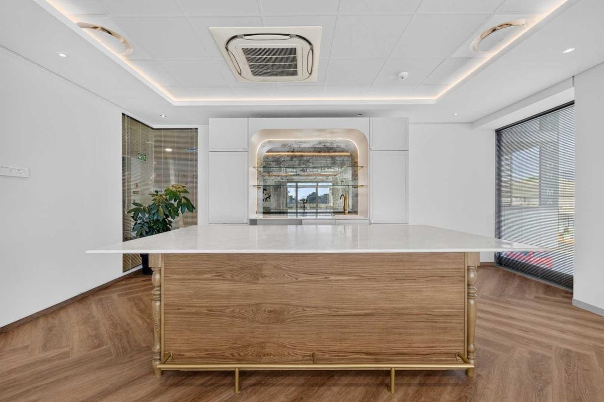 Modern office kitchenette featuring a central wooden island with a stone countertop, integrated cabinetry, and recessed ceiling lighting.