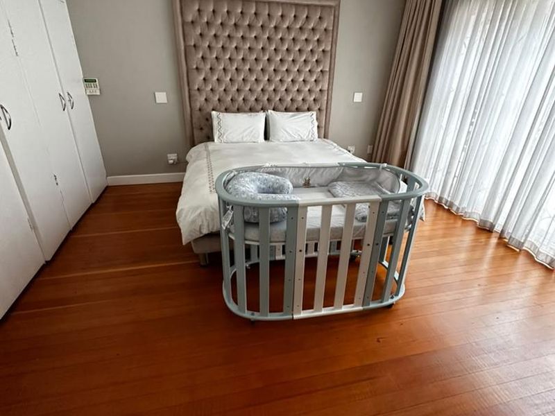 Spacious bedroom featuring polished hardwood flooring, built-in cabinetry, and a wall-mounted air conditioning unit, offering a comfortable and well-maintained living space.