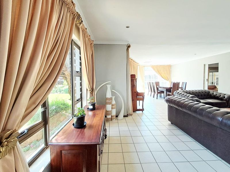 Spacious open-plan living and dining area featuring neutral tiled flooring, recessed lighting, and large windows with garden views.