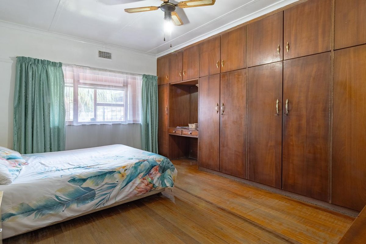 A bedroom featuring extensive built-in wooden cabinetry with integrated desk space, timber flooring, and a ceiling fan.