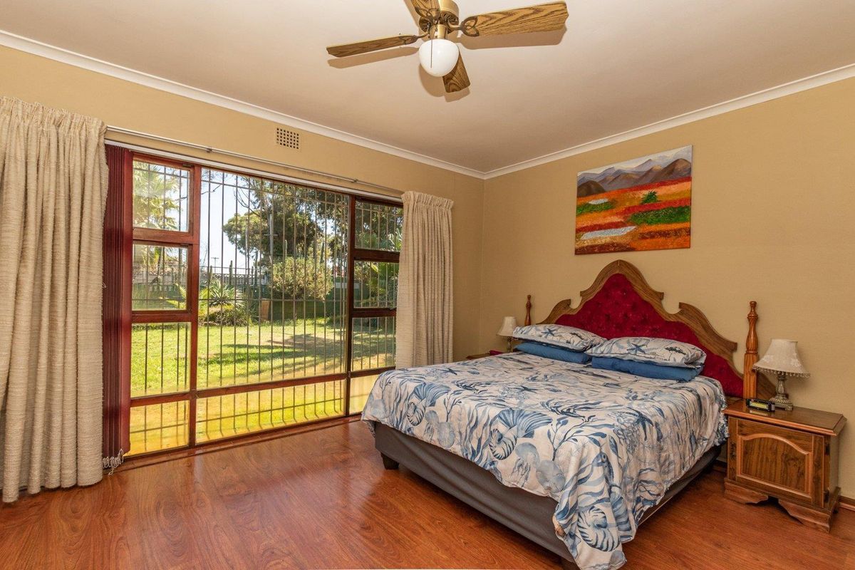 Spacious bedroom featuring laminate flooring, a ceiling fan, and large windows with security bars overlooking the garden.
