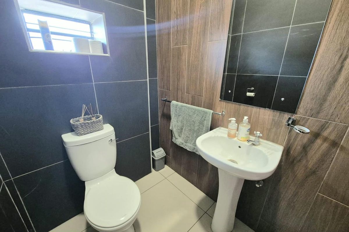 A modern bathroom featuring dark grey and wood-look wall tiles, a white pedestal basin, and a standard toilet.