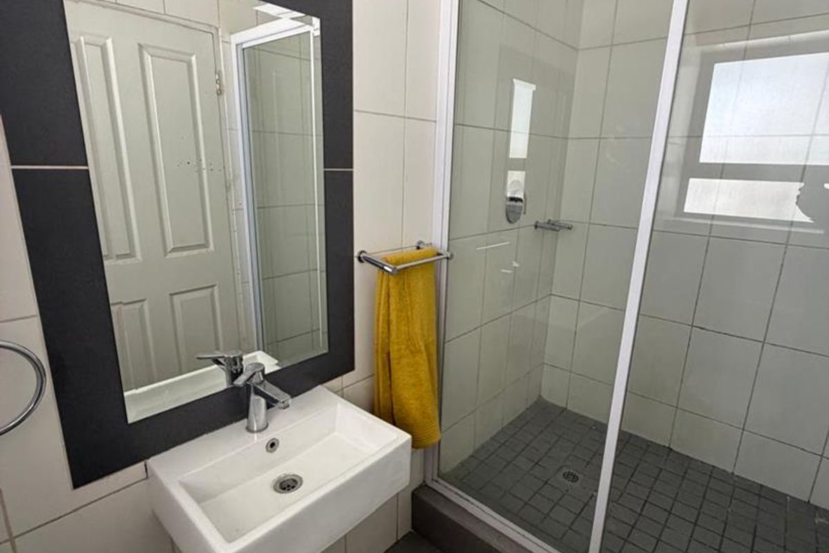 A functional bathroom featuring a wall-mounted basin, a framed mirror, and a glass-enclosed shower with tiled flooring.