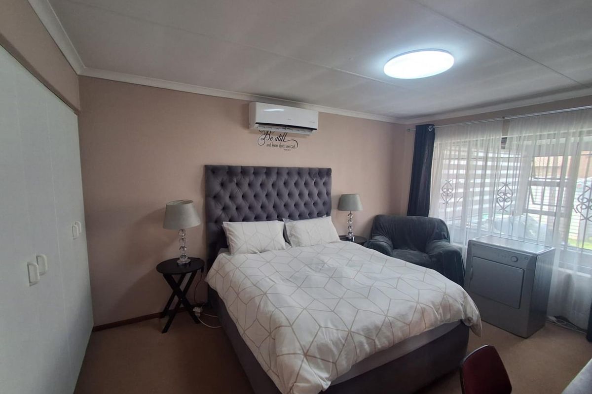 A well-lit bedroom featuring built-in cupboards, a wall-mounted air conditioning unit, and large windows allowing for natural light.