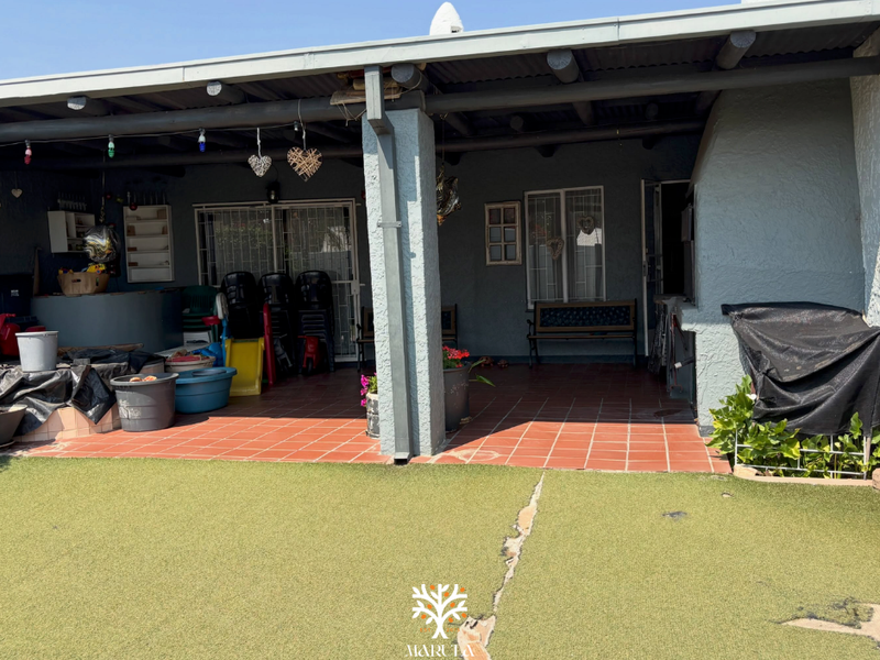 A covered outdoor patio area featuring tiled flooring, a built-in braai, and direct access to the garden through sliding doors.