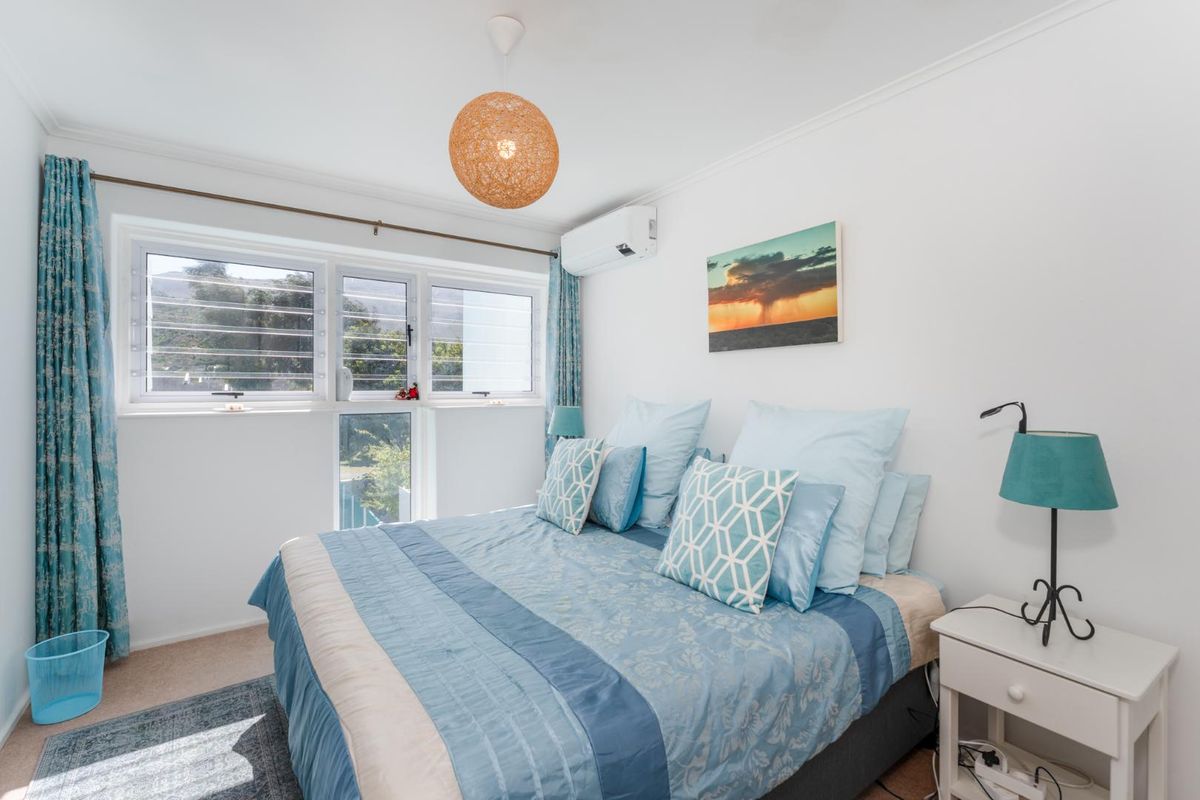 A bright and well-maintained bedroom featuring louvered windows, carpeted flooring, and a wall-mounted split-system air conditioning unit.