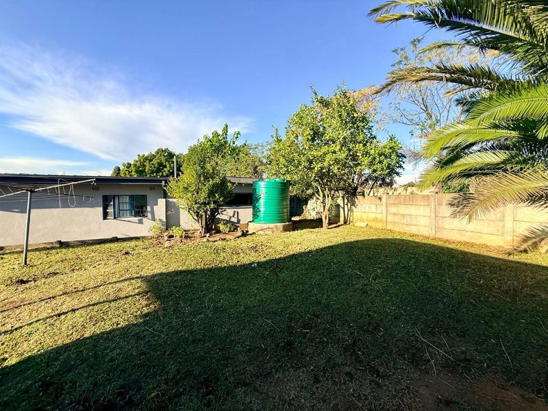A spacious rear garden featuring a lawn, mature trees, a water storage tank, and a secure precast concrete boundary wall.
