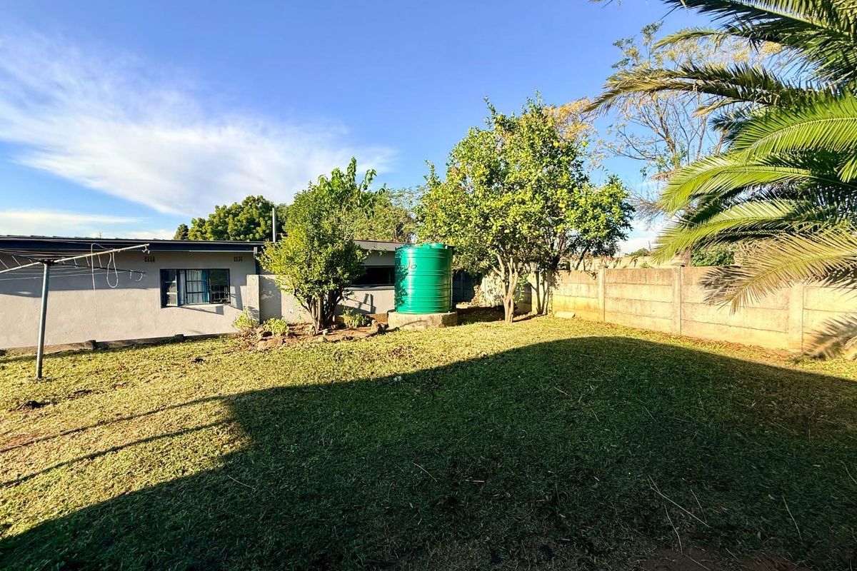 A spacious rear garden featuring a lawn, mature trees, a water storage tank, and a secure precast concrete boundary wall.