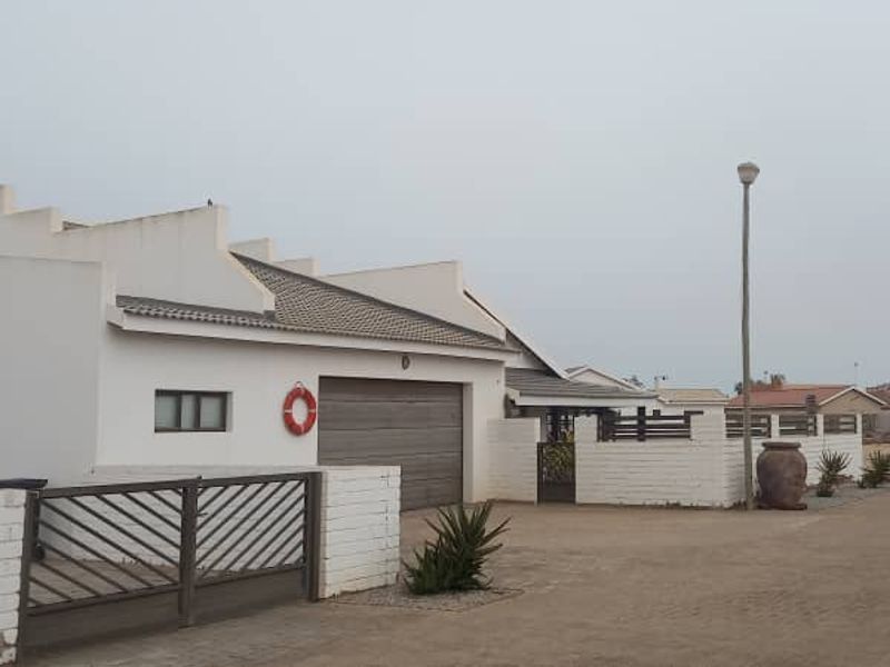 Front exterior view of the property featuring a single garage, white boundary walls, and a metal entrance gate.