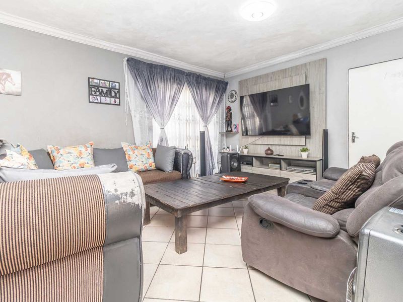 A comfortable living room featuring tiled flooring, decorative coving, and a built-in media wall unit for entertainment.