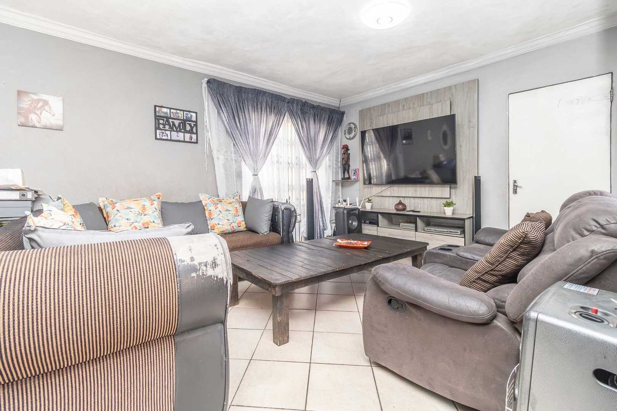 A comfortable living room featuring tiled flooring, decorative coving, and a built-in media wall unit for entertainment.