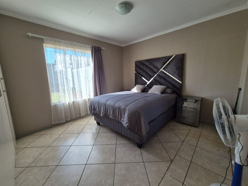 A well-lit bedroom featuring neutral wall tones, tiled flooring, and a built-in cupboard, providing a functional and comfortable living space.