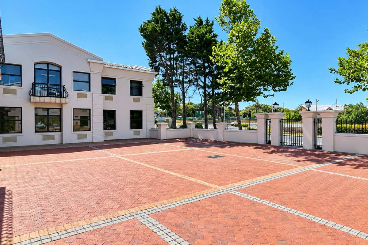 A well-maintained exterior courtyard featuring brick paving, perimeter walling with iron gates, and a multi-story office building facade.