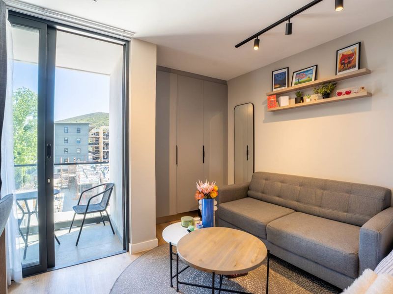 Modern living area featuring built-in cupboards, sleek track lighting, and direct access to a private balcony through large sliding glass doors.