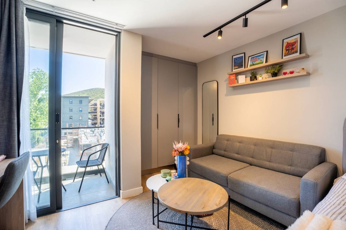 Modern living area featuring built-in cupboards, sleek track lighting, and direct access to a private balcony through large sliding glass doors.