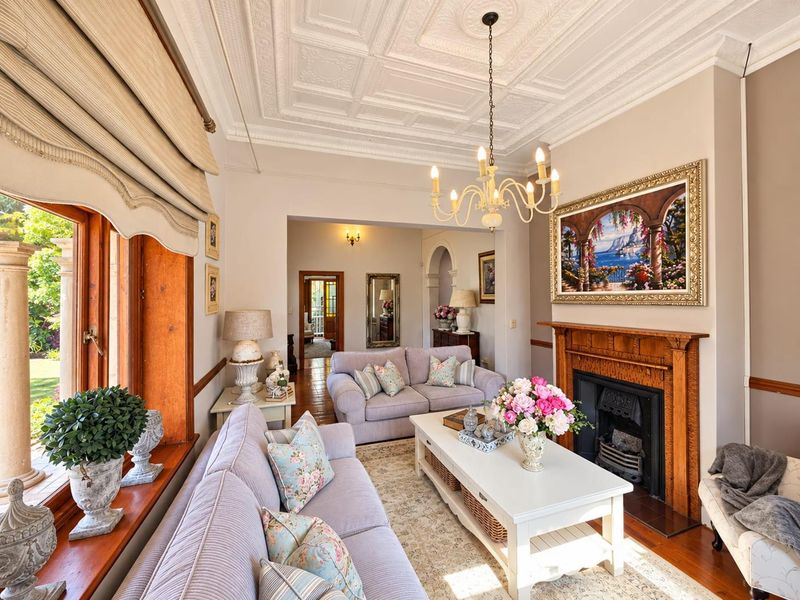 Elegant living room featuring a classic timber fireplace, ornate pressed metal ceiling, and polished timber flooring with views toward the garden.